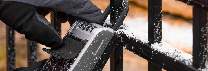 A person wearing winter gloves accesses a lock box in the snow