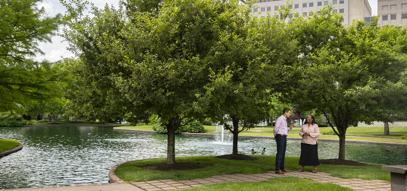 two people talking under trees near water