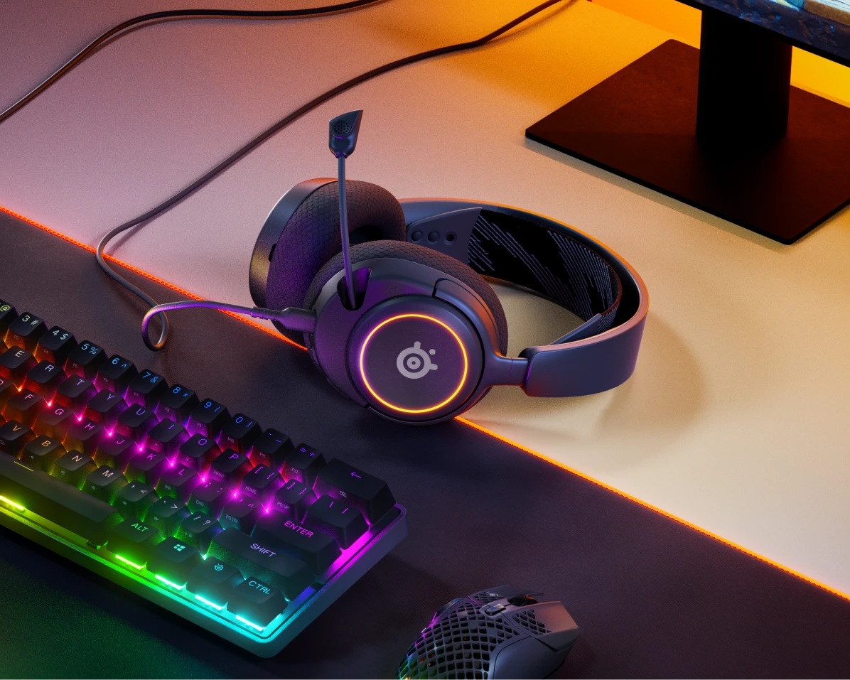 Arctis Nova 3 laying on the desk accompanied with keyboard, mousepad and gaming mouse, with an orange glow emanating from beneath the monitor, which is in the background.