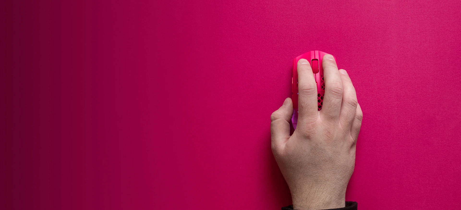 Top-down view of a hand using a matching magenta pink SteelSeries Aerox gaming mouse on a custom magenta-colored surface, highlighting color synchronization for gaming setups.