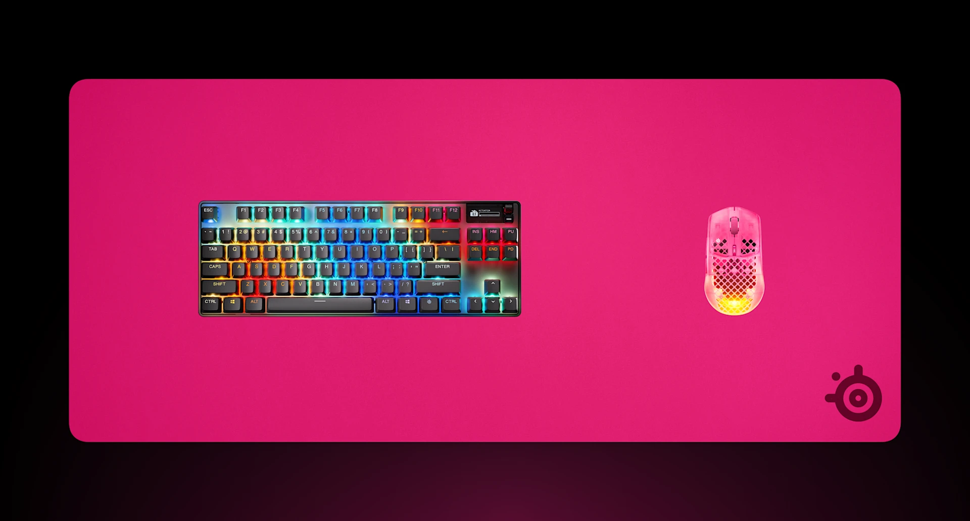 Vista desde arriba de una alfombrilla para ratón de gaming SteelSeries QcK Heavy XXL en color magenta, con un teclado mecánico RGB y un ratón de gaming Aerox también en magenta.