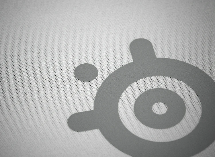 Extreme close-up of the high thread count micro-woven cloth surface on the white SteelSeries QcK Heavy XXL, optimized for both optical and laser sensor tracking accuracy.