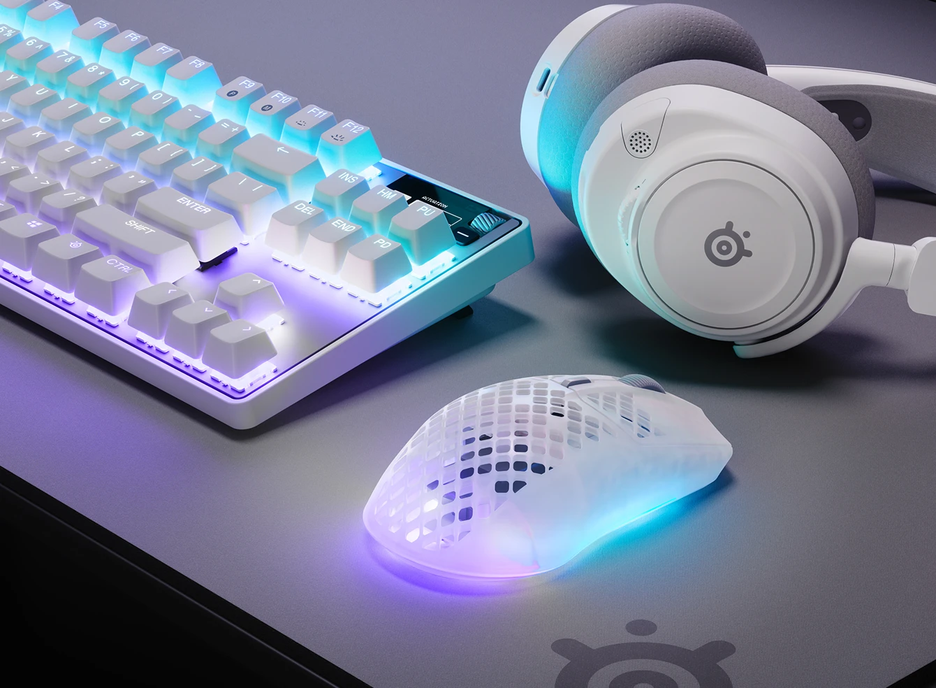 Teclado RGB, auriculares y ratón para juegos translúcido sobre un escritorio con iluminación morada y azul.