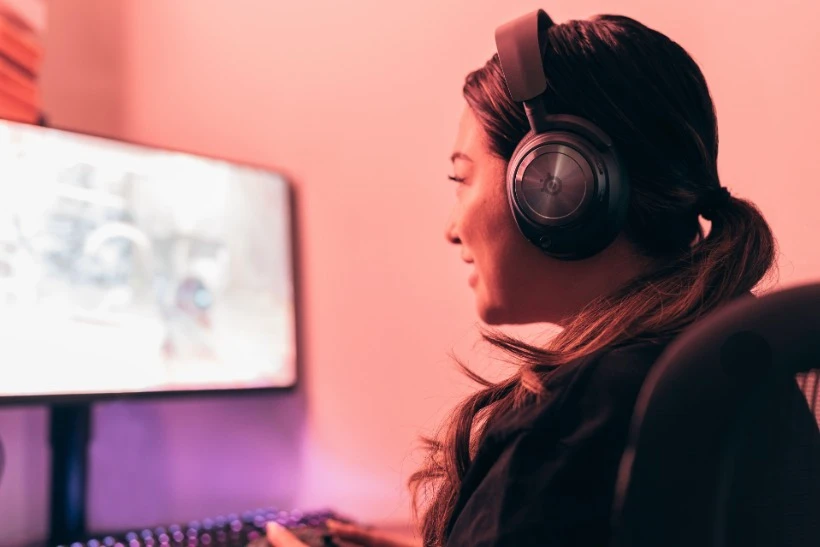 View on a woman from the side, she is wearing a headset and she is playing with gaming pad.