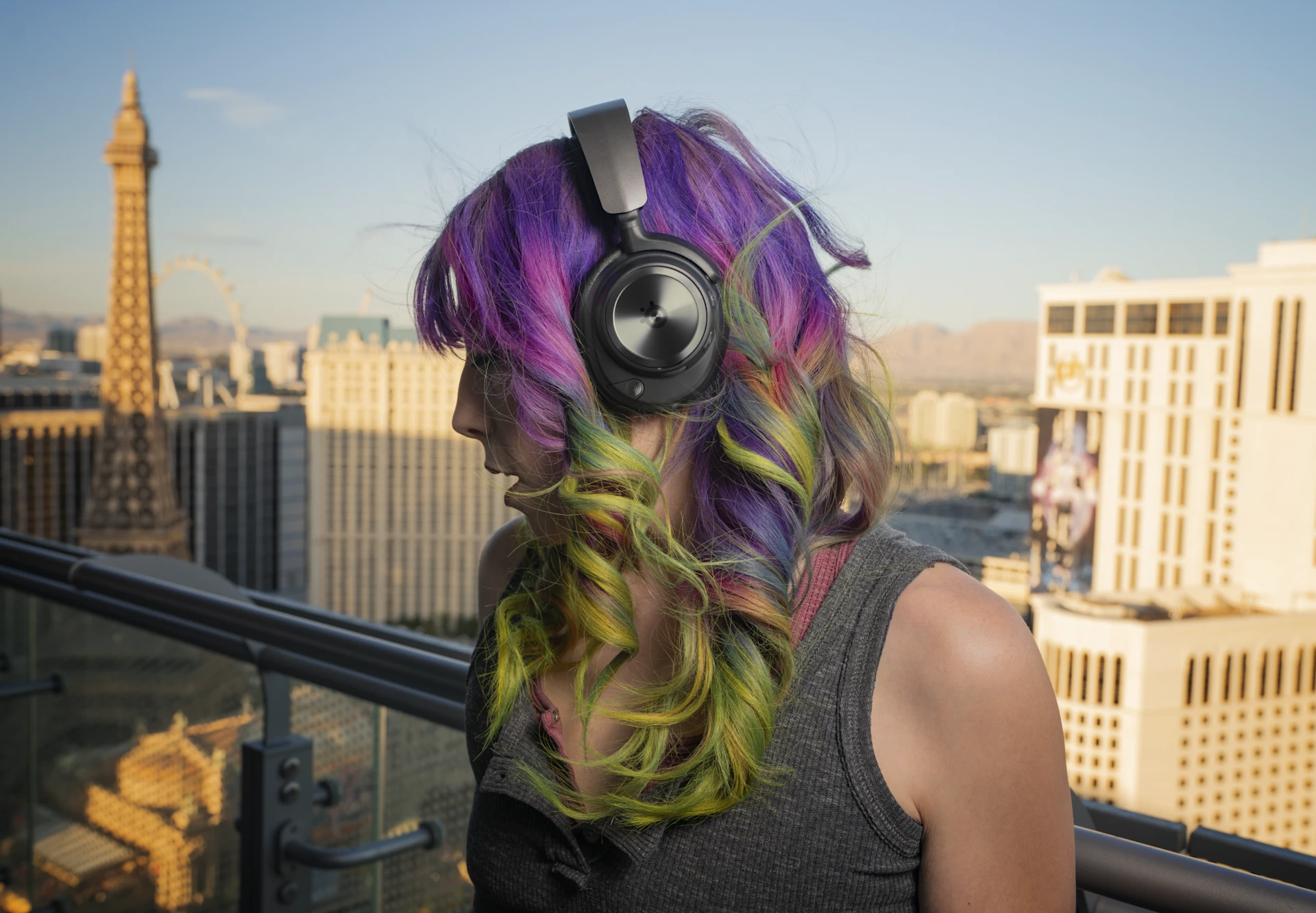 Woman in colorful hair standing on the balcony, wearing a black headset with a Las Vegas background.