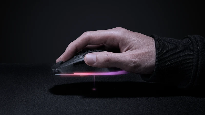 Hand resting on low‑profile gaming mouse with subtle pink sensor glow on mousepad.
