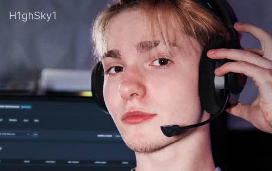 A young man wearing black Arctis Nova 5 headsets, with the microphone pulled out, looking directly into the camera.