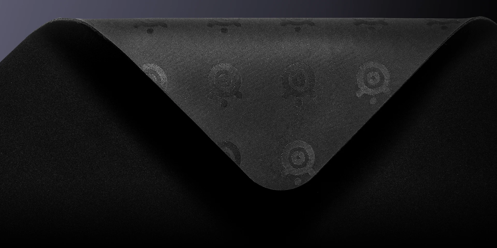 La esquina de una alfombrilla de ratón negra está despegada, dejando al descubierto una base de goma antideslizante con un patrón repetitivo del logotipo de SteelSeries.