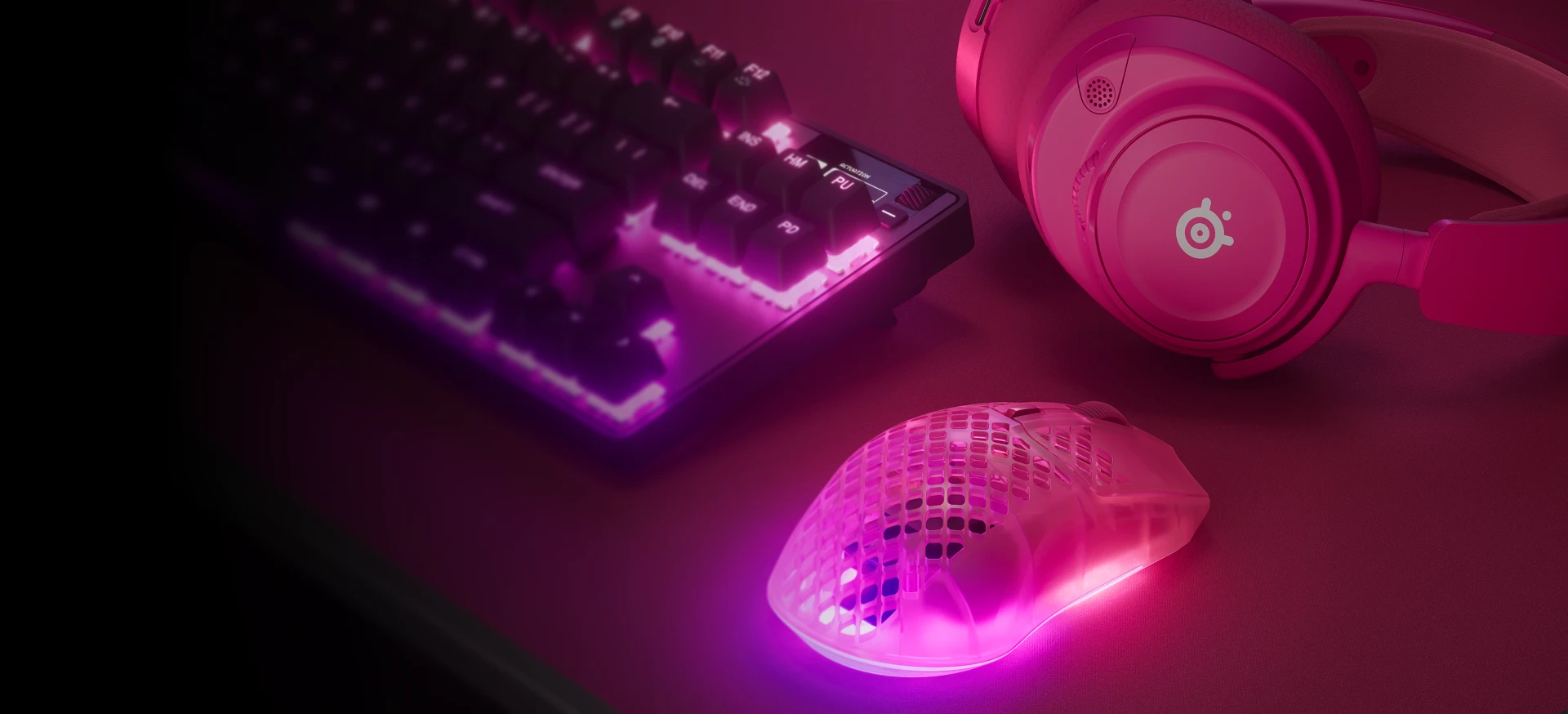 RGB keyboard, headset, and translucent gaming mouse on a desk in purple-blue lighting.