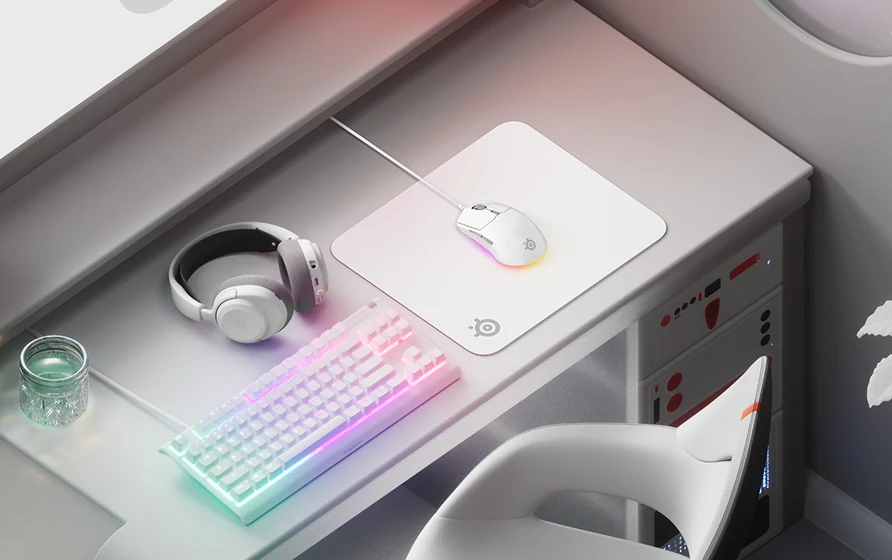 Elegantná biela herná zostava s RGB klávesnicou, svietiacou myšou na bielej podložke SteelSeries a ladiacimi bielymi slúchadlami na modernom stole.