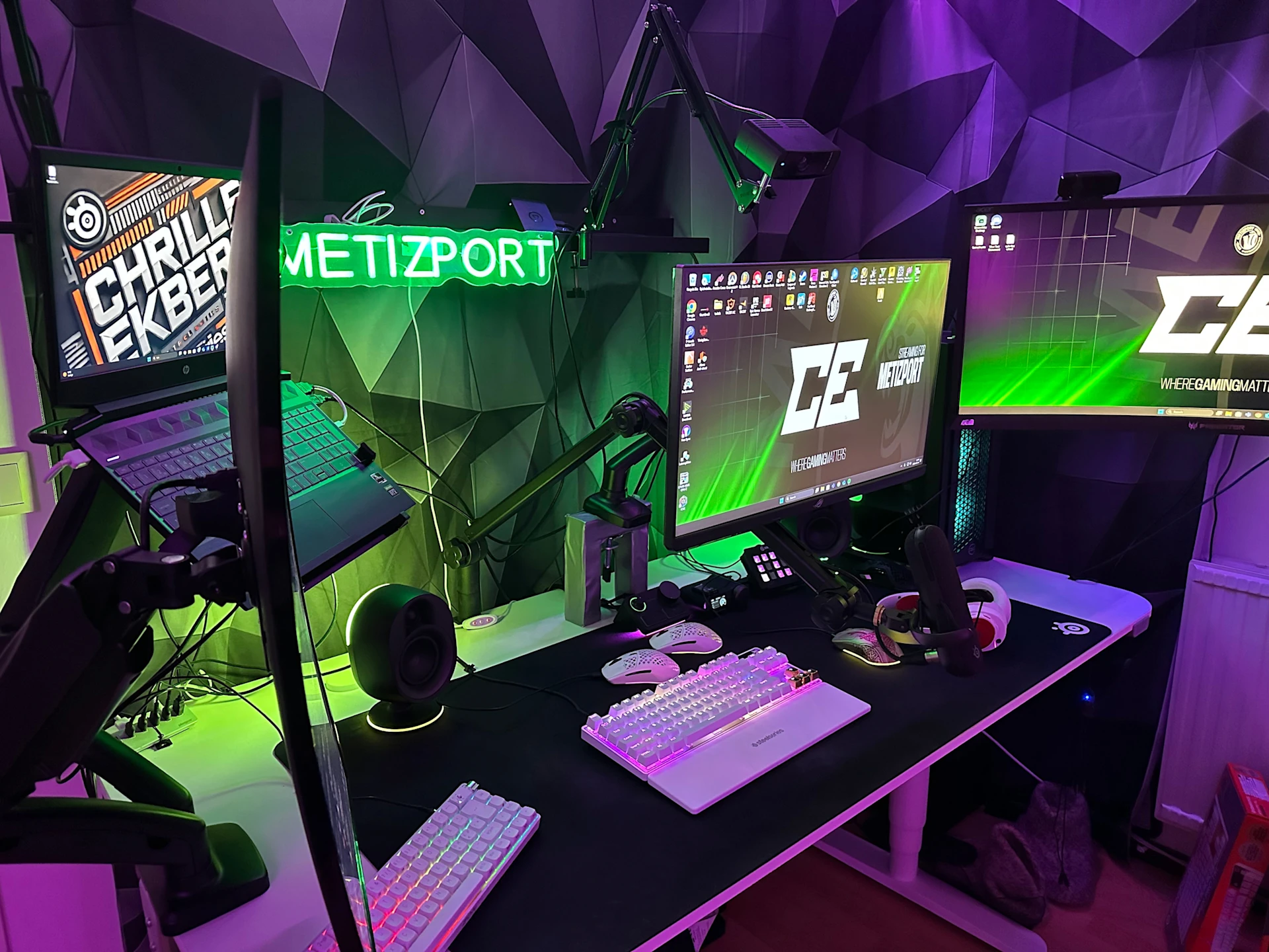 a High-tech Setup with 4 screen and bathed in purple and green RGB lighting, featuring white SteelSeries Devices.