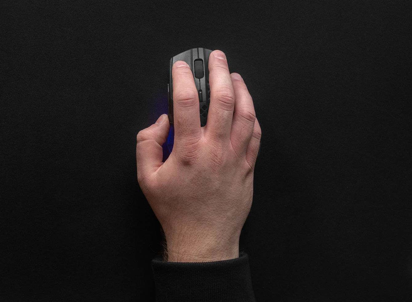 Vista de cima de uma mão usando um mouse de gaming preto sobre um mousepad QcK grande e liso, também preto.