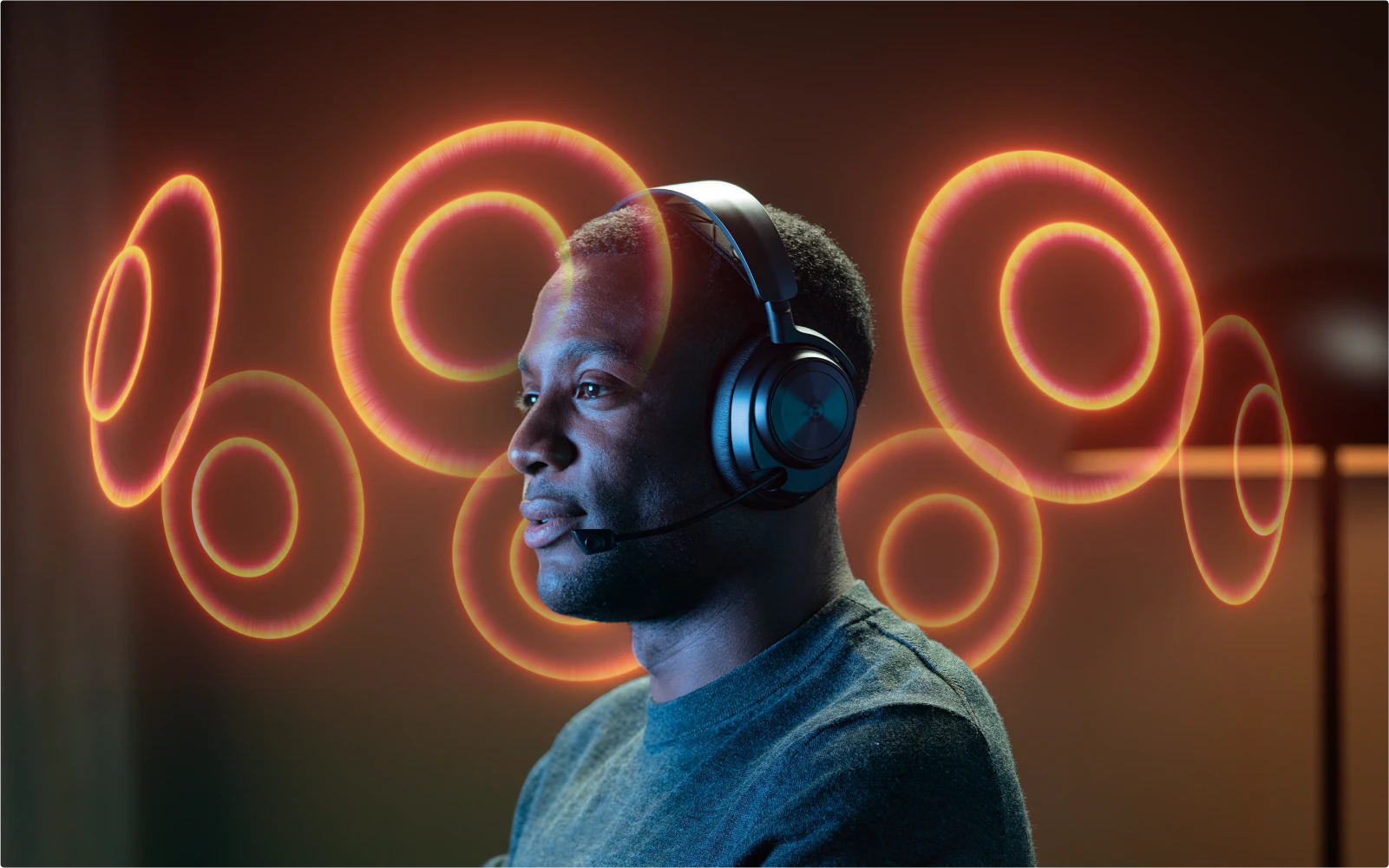A man sitting in Arctis Nova Pro headphones, surrounded by floating orange semicircles symbolizing the acoustic space.
