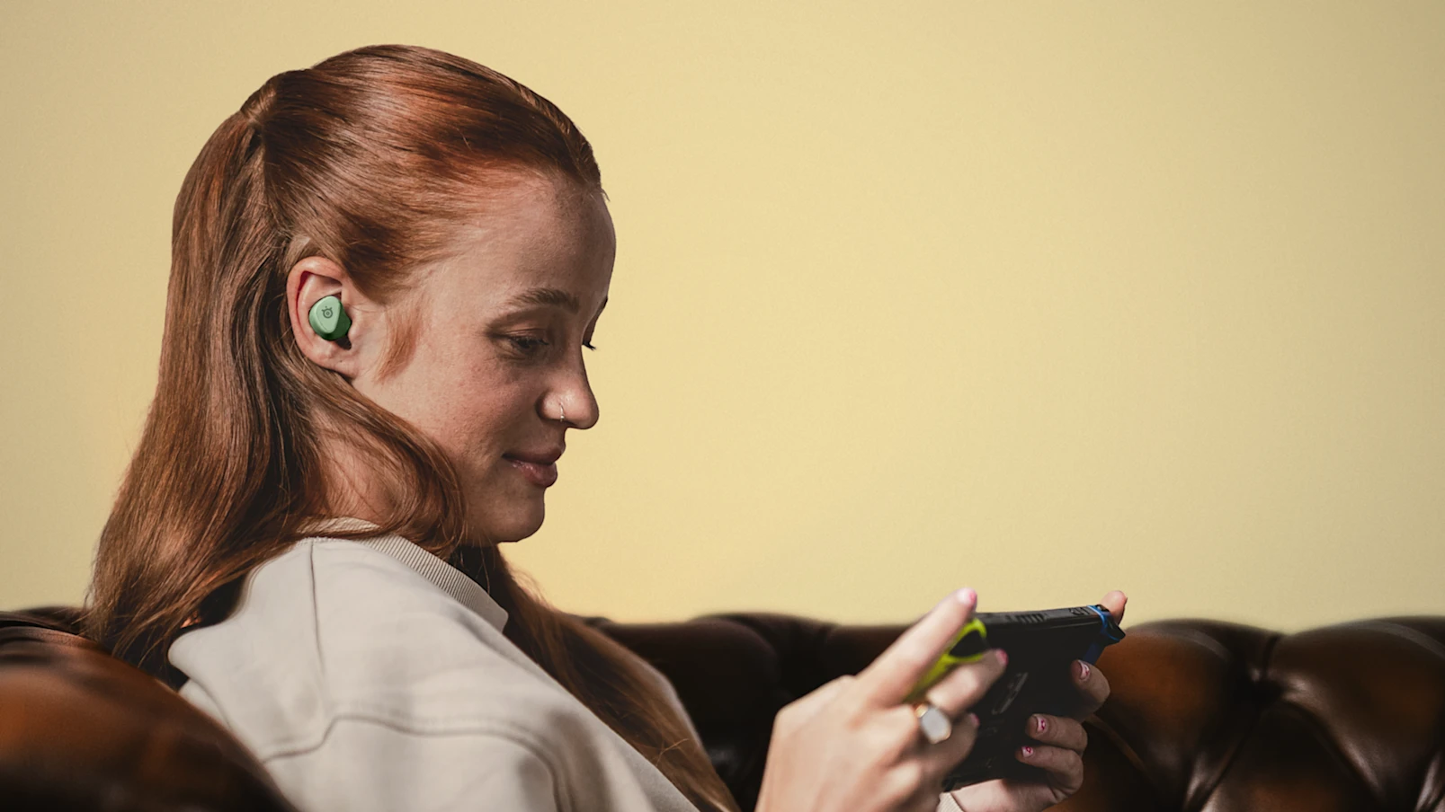 Gamer wearing a matcha green SteelSeries Arctis GameBud while playing on a handheld gaming console.