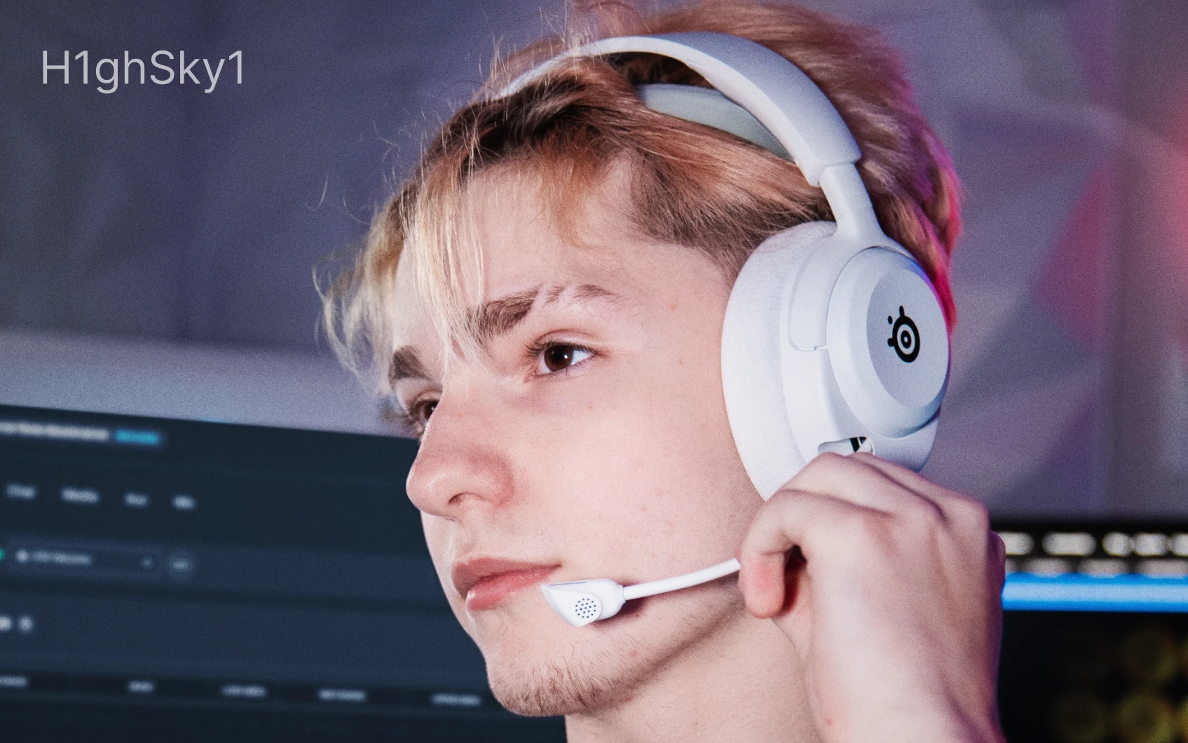 A young man wearing White Arctis Nova 5 headsets, with the microphone pulled out, looking sideway.
