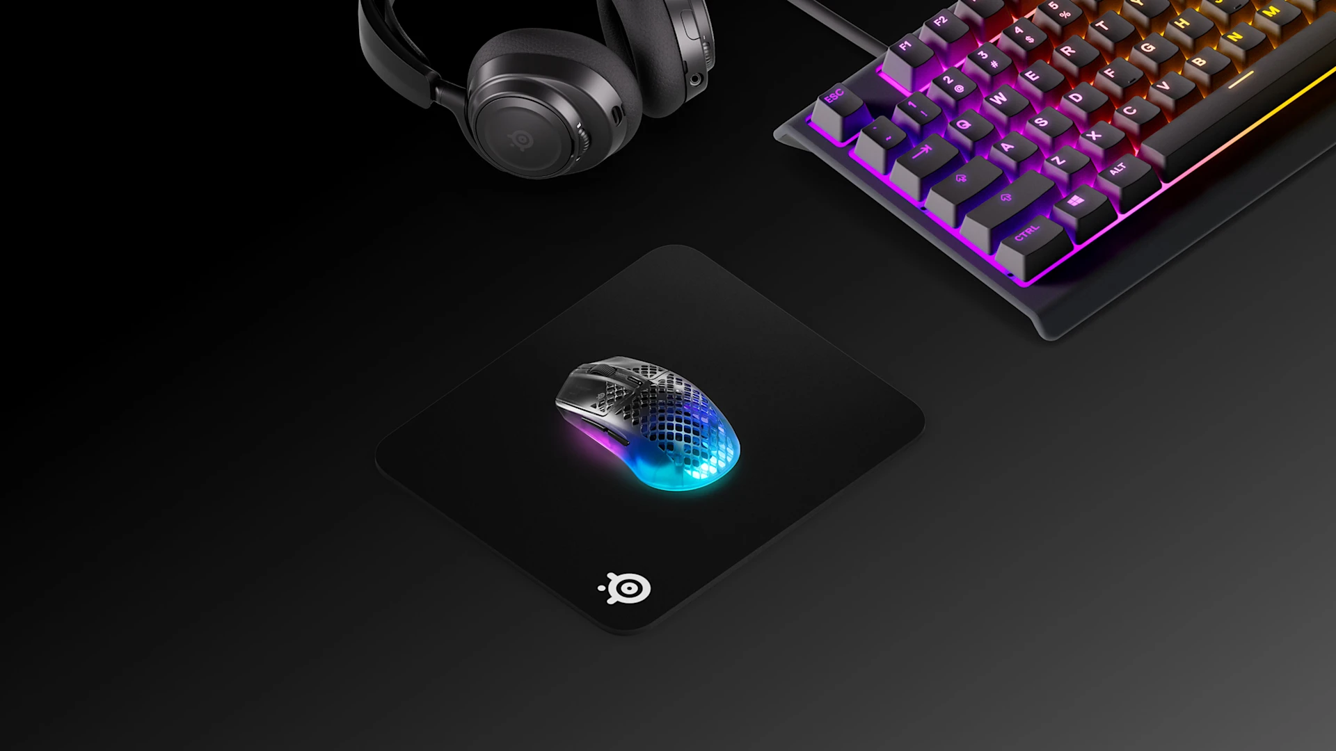 Vista isométrica de uma configuração clássica de jogos SteelSeries em preto, com o mousepad QcK Heavy M, o teclado Apex RGB, o headset Arctis Nova e o mouse Aerox 3 Wireless.
