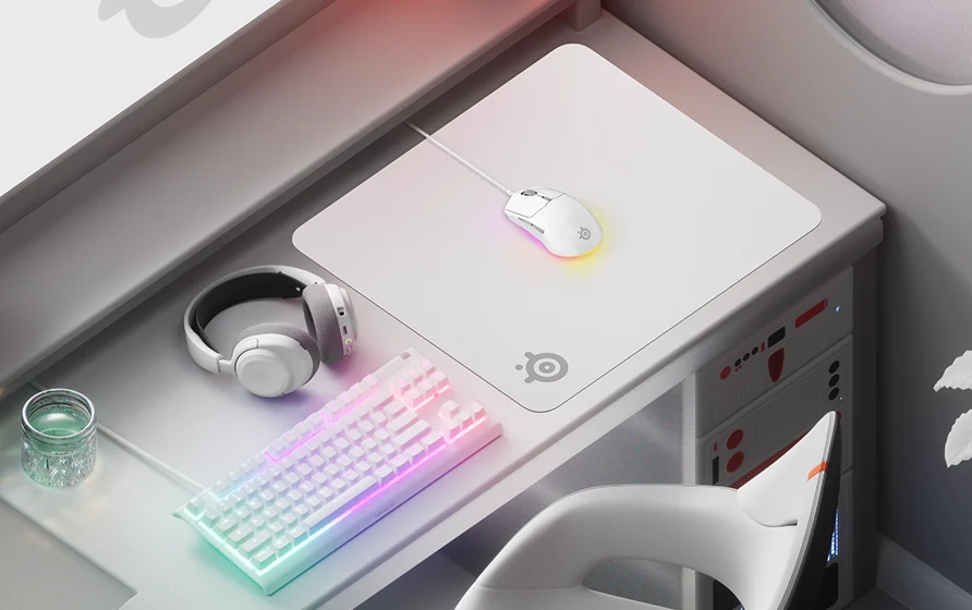 En elegant, vit speluppsättning med ett RGB-tangentbord, en lysande mus på en vit SteelSeries-musmatta och matchande vita hörlurar på ett modernt skrivbord.