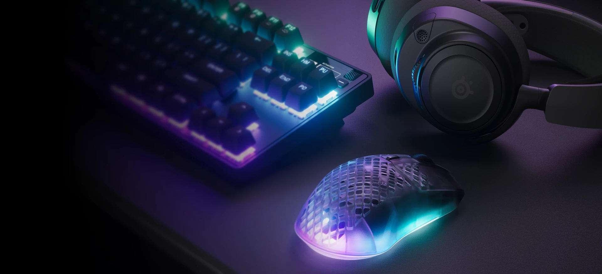 RGB keyboard, headset, and translucent gaming mouse on a desk in purple-blue lighting.
