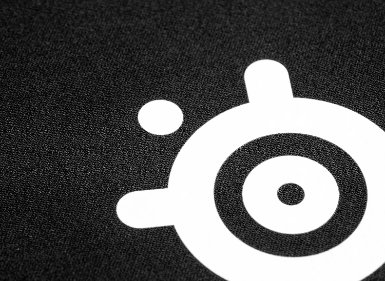 Close-up extremo da superfície de tecido micro-tecido de alta densidade de um mousepad preto da SteelSeries, com o logotipo da SteelSeries em branco nítido.