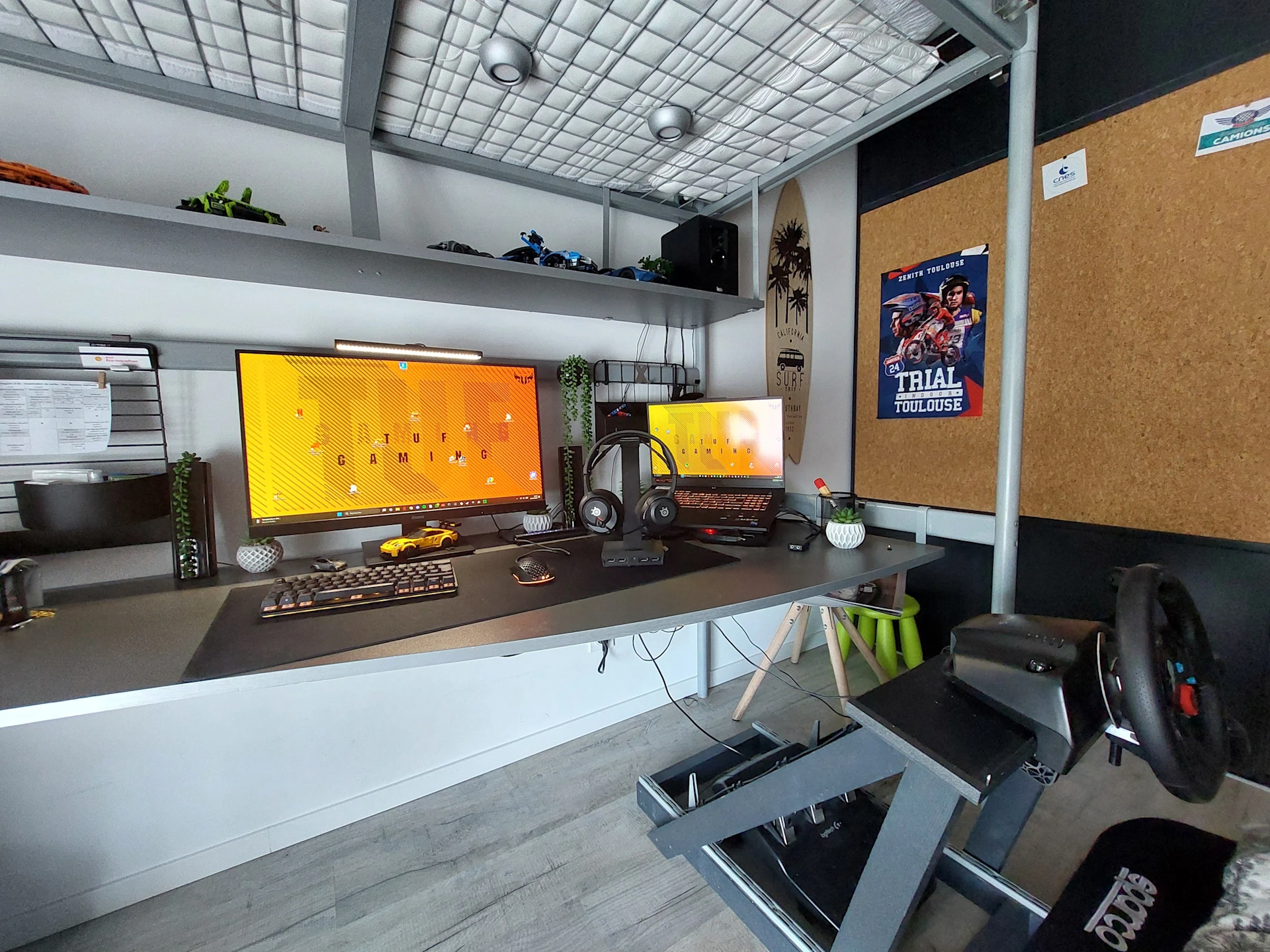 A vertical dual-monitor gaming setup with a orange wallpaper, featuring SteelSeries Devices and a steering wheel for race games.