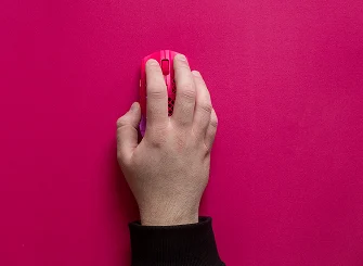 Vista desde arriba de una mano utilizando un ratón para juegos SteelSeries Aerox en rosa magenta a juego sobre una superficie personalizada de color magenta, destacando la sincronización de colores para las configuraciones de juego.