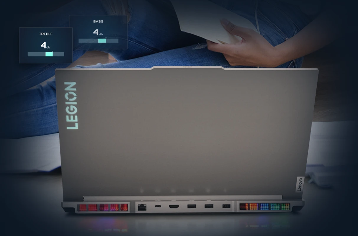 The back of a grey Lenovo Legion gaming laptop with the logo illuminated. Overlays show sound settings for "TREBLE" and "BASS."