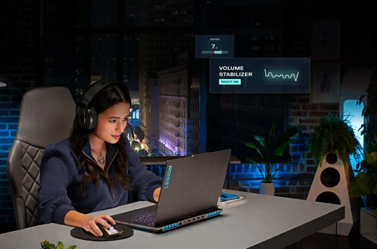 A woman wearing headphones focuses on her Lenovo Legion laptop in a room at night. An overlay shows the "VOLUME STABILIZER" feature is on.