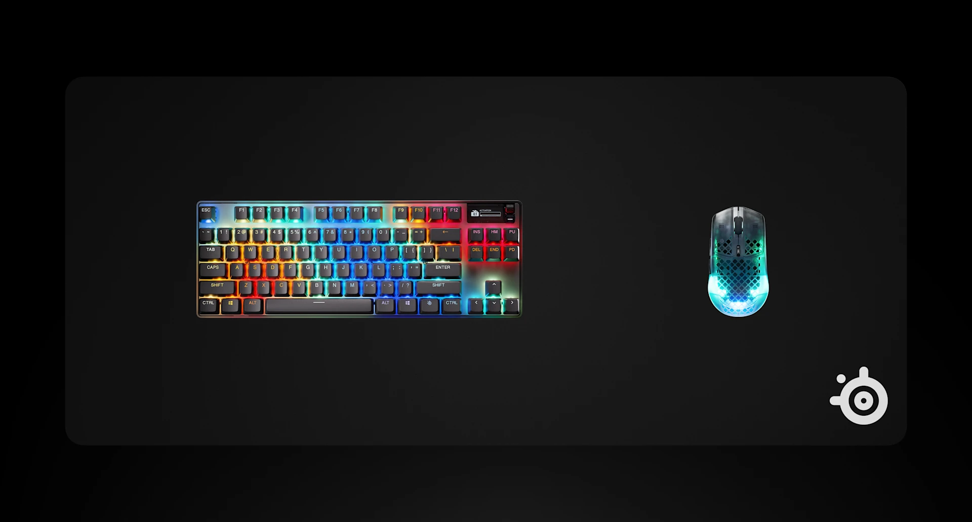 A mechanical gaming keyboard with RGB backlighting alongside a SteelSeries mousepad and a glowing, translucent gaming mouse on a black background.