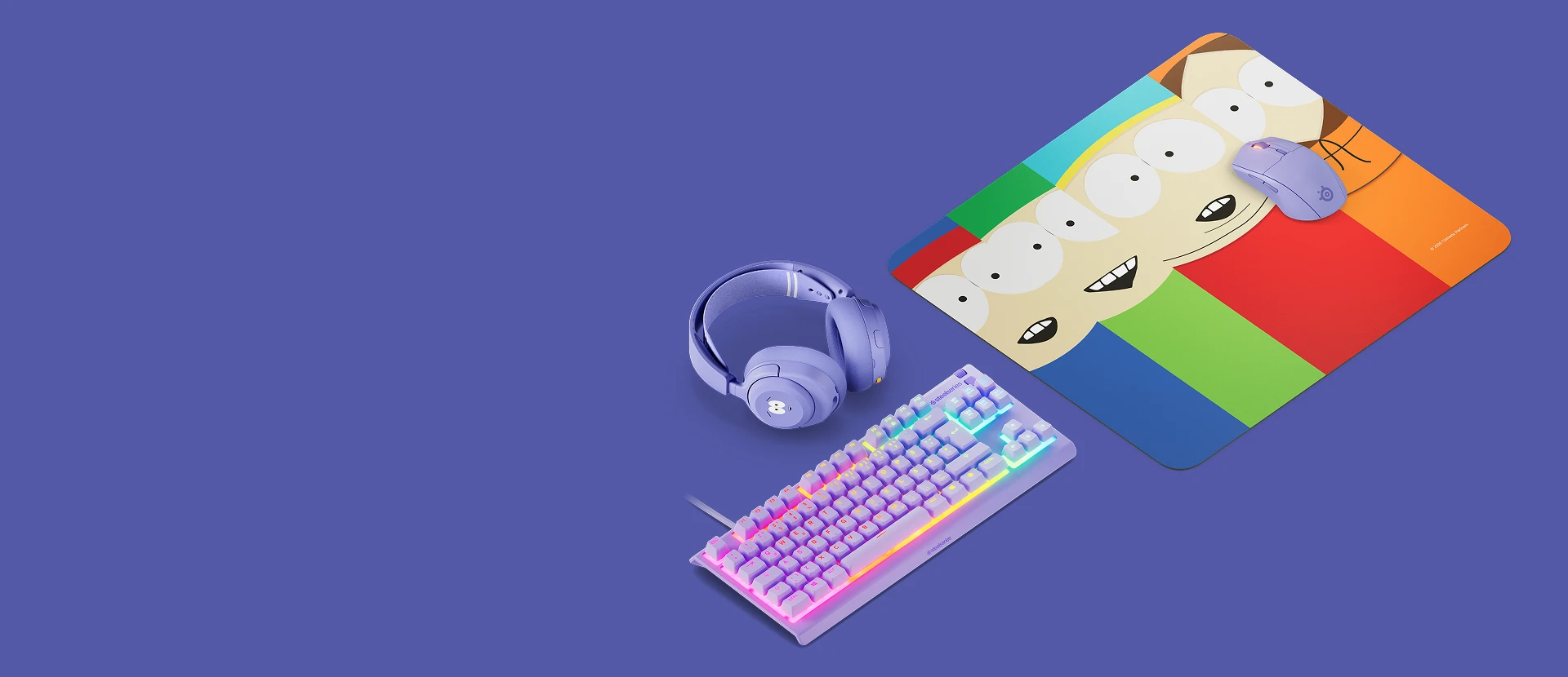 SteelSeries South Park gaming setup featuring a QcK mousepad with Stan, Kyle, Cartman, and Kenny, purple wireless mouse, headset, and RGB keyboard.