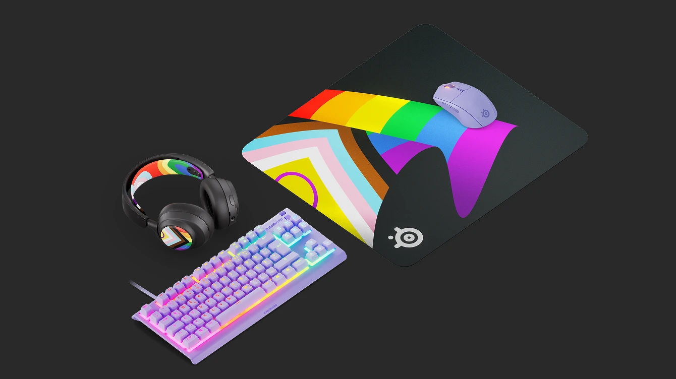 SteelSeries gaming setup featuring the Arctis Nova headset, Apex keyboard, and Aerox mouse with the limited edition QcK L Pride 2026 rainbow mousepad.
