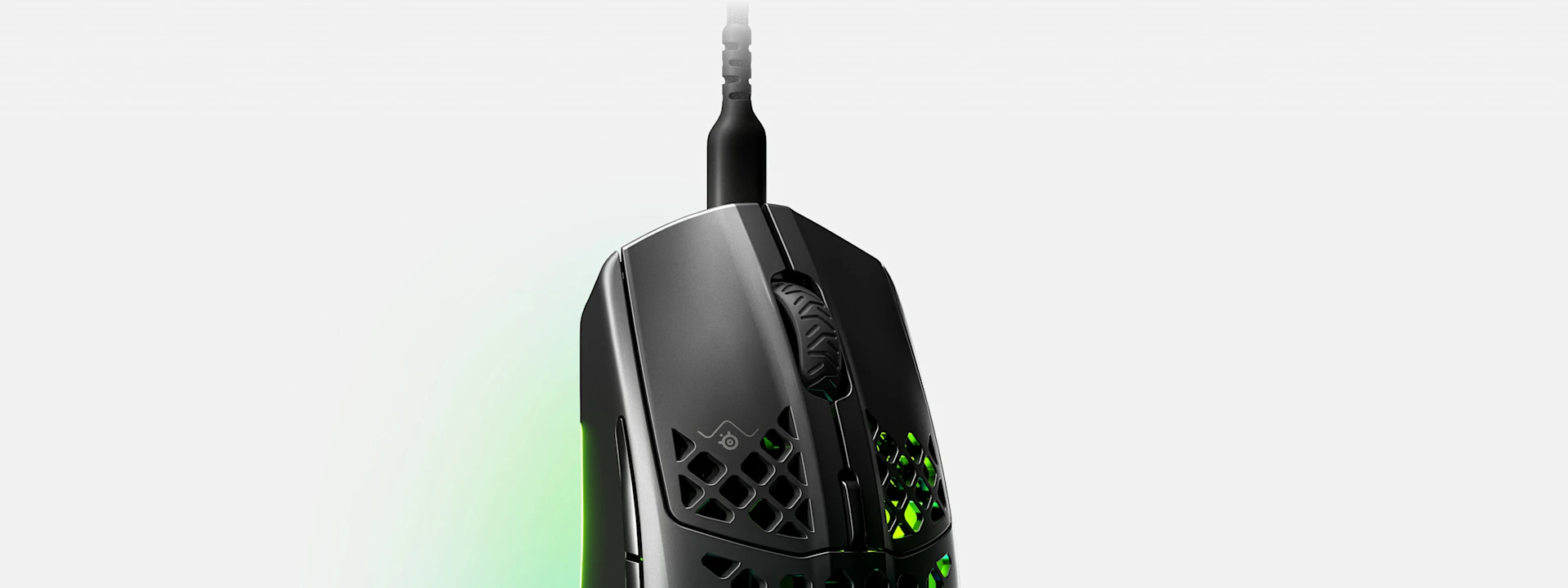 A close-up of a black gaming mouse with a honeycomb design and green light glowing from inside.