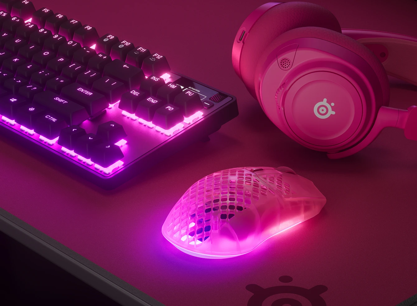 RGB keyboard, headset, and translucent gaming mouse on a desk in purple-blue lighting.