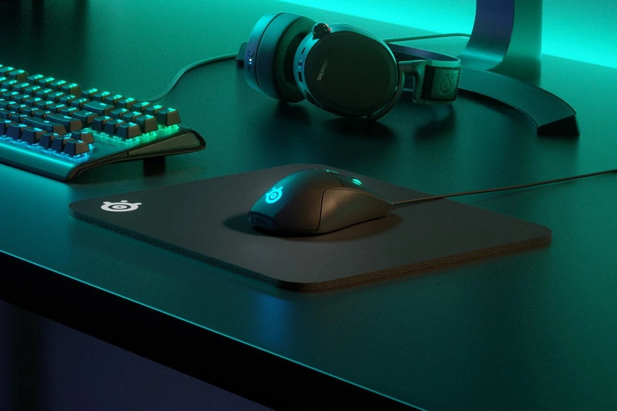 Mouse pad placed on the desk with keyboard, headphones and computer mouse surrounded by green light. 