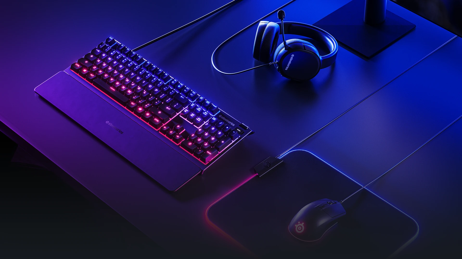 A SteelSeries gaming set with a keyboard, mouse, and headset, all featuring vibrant green and purple RGB lighting on a desk.