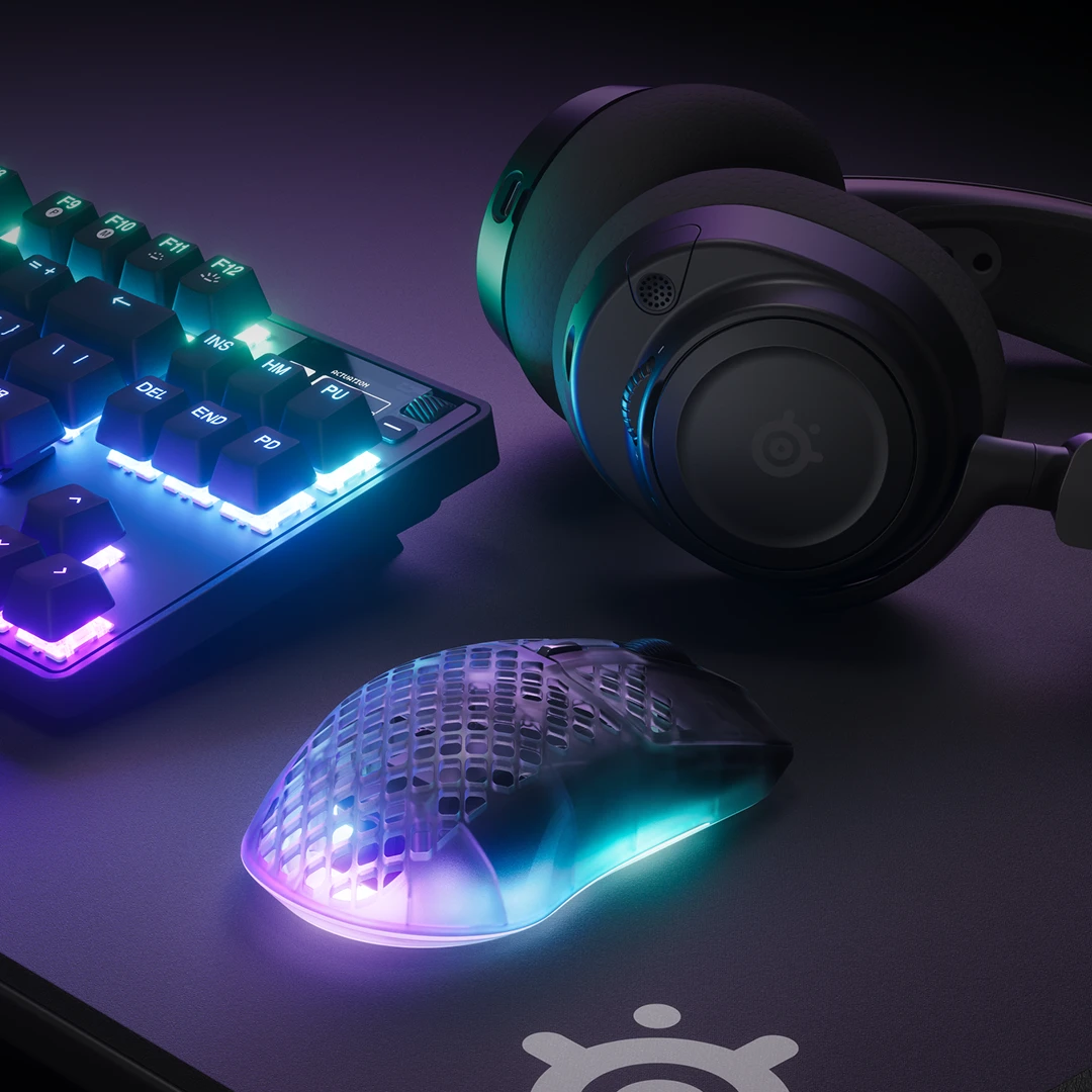 SteelSeries-gamingopstelling met het Apex Pro TKL-toetsenbord, de Arctis Nova Pro Wireless-headset en de Aerox 3-muis met gesynchroniseerde PrismSync RGB-verlichting op een QcK-muismat.