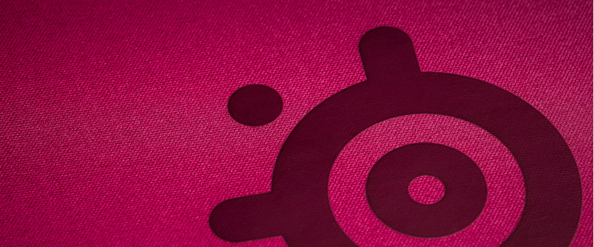 Primerísimo primer plano de la superficie de tela microtejida de alta densidad del SteelSeries QcK Heavy XXL en color magenta, optimizada para la precisión de seguimiento tanto de sensores ópticos como láser.