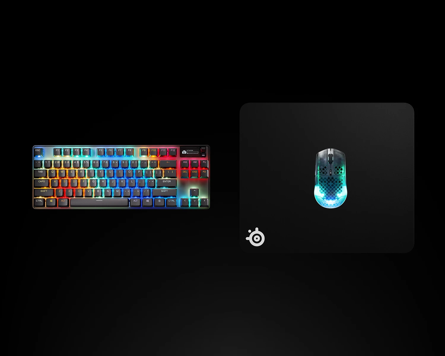 Mechaniczna klawiatura gamingowa z podświetleniem RGB obok podkładki SteelSeries i świecącej, półprzezroczystej myszki gamingowej na czarnym tle.