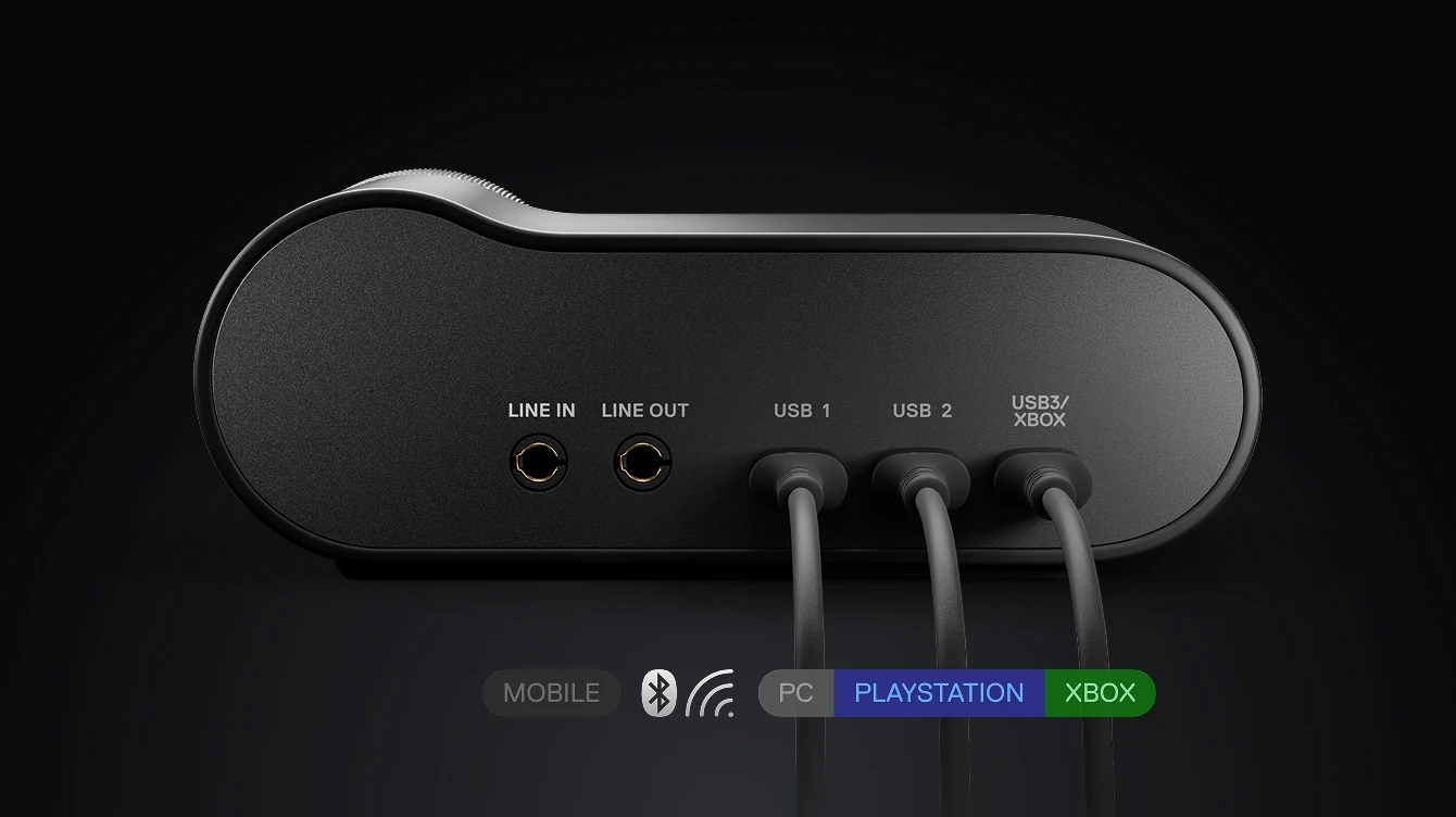 Pohled zezadu na herní audio základnu s vstupem, výstupem, třemi USB porty a ikonami platforem pro PC, PlayStation, Xbox a mobilní zařízení.