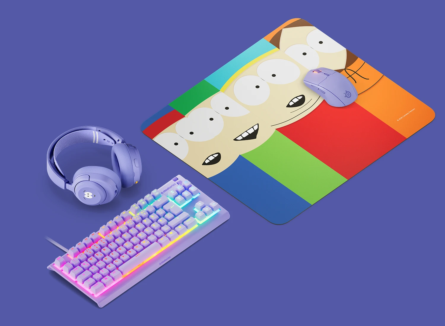 SteelSeries South Park gaming setup featuring a QcK mousepad with Stan, Kyle, Cartman, and Kenny, purple wireless mouse, headset, and RGB keyboard.
