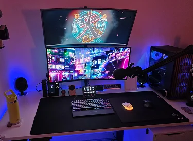 tacked dual monitors with a cyberpunk theme, featuring a boom arm mic, Stream Deck, and mechanical keyboard on a desk mat with vibrant blue ambient lighting.