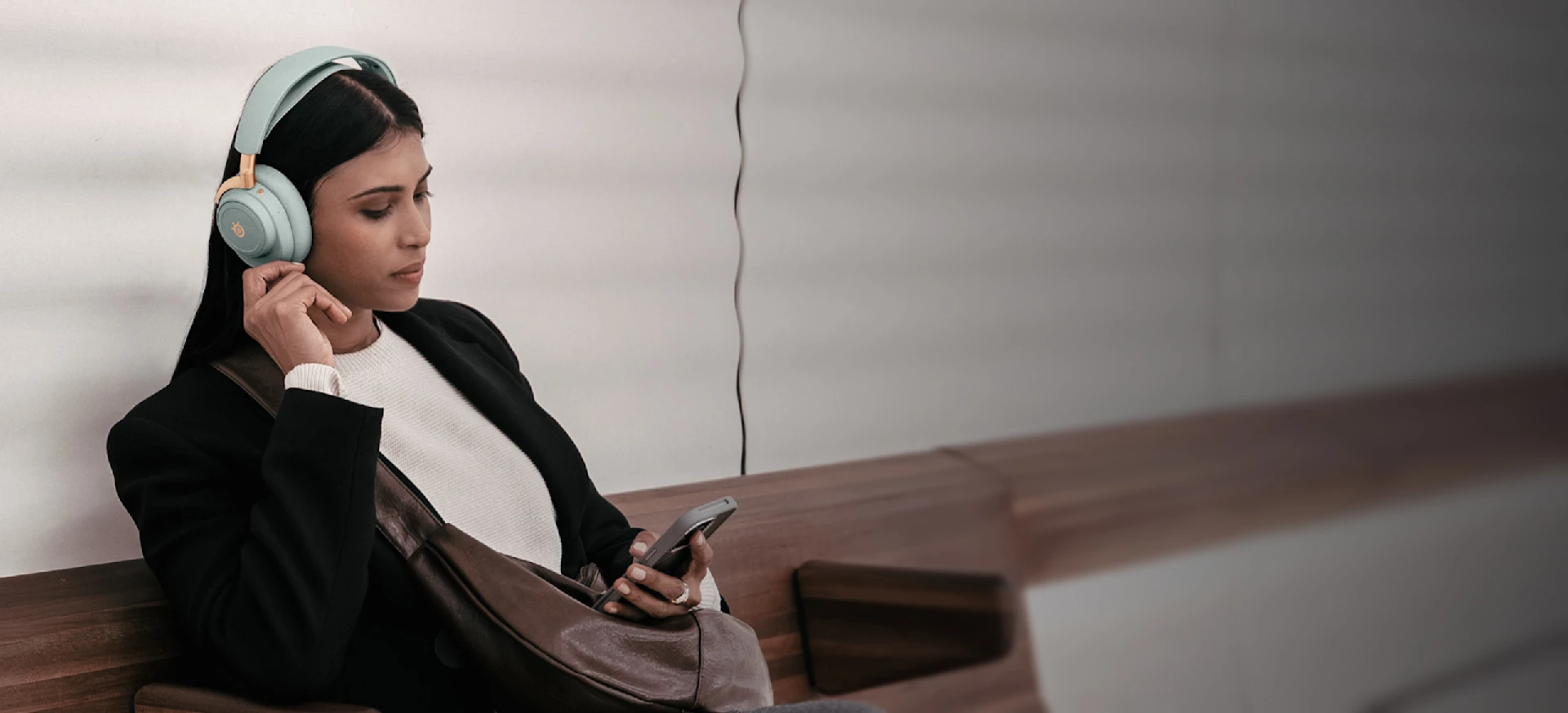 Caucasian woman sitting on a bench wearing Arctis Nova Elite headset
