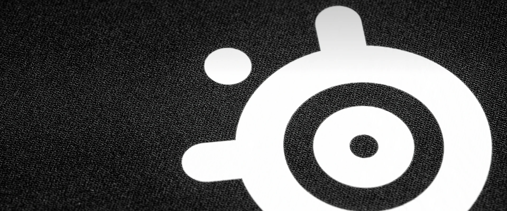 Close-up extremo da superfície de tecido micro-tecido de alta densidade de um mousepad preto da SteelSeries, com o logotipo da SteelSeries em branco nítido.