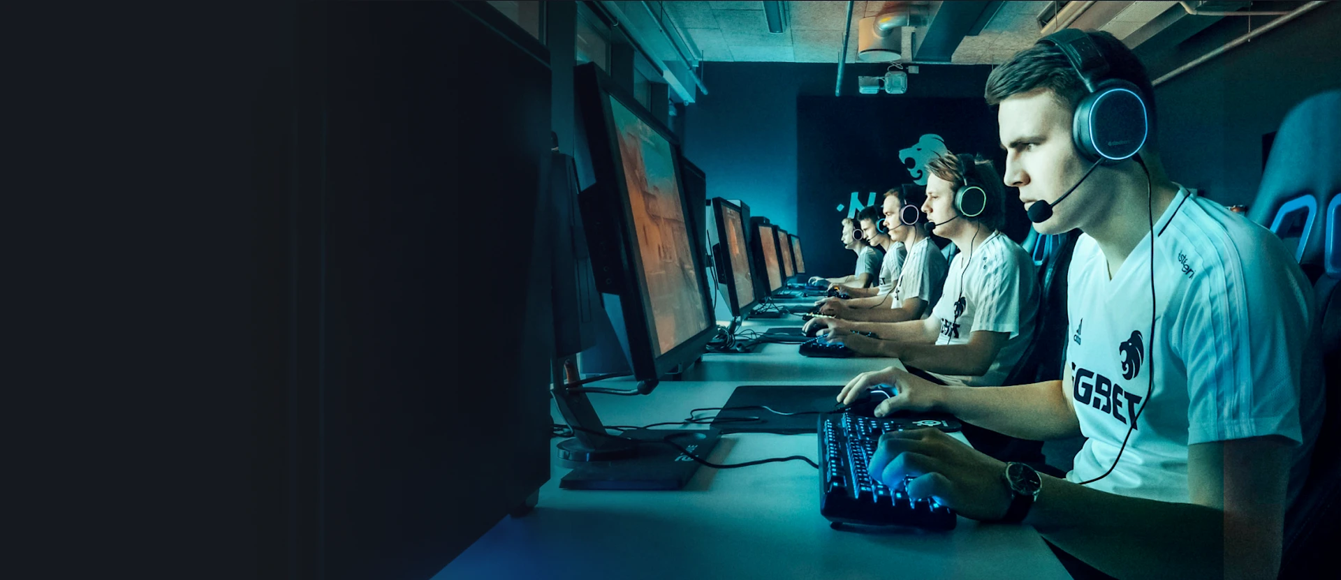 A team of professional esports players in matching jerseys, sitting in a row and intensely focusing on their computer screens during a tournament.