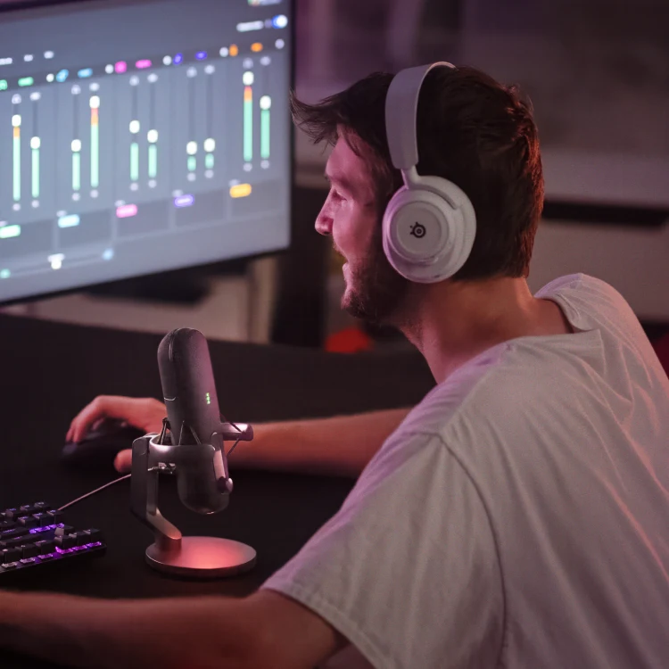 A man playing on a computer using headphones and a microphone surrounded by orange light.