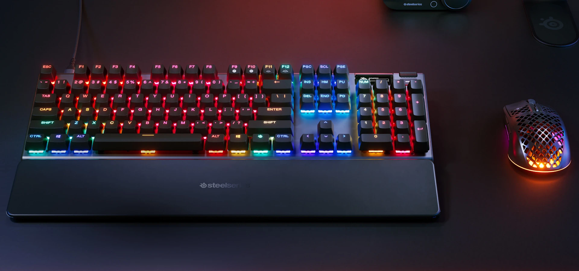 Teclado Apex Pro Gen 3 iluminado com cores RGB, com um mouse iluminado com RGB ao lado.