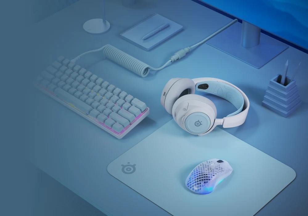 A stylish gaming setup with a white mechanical keyboard, headset, and mouse on a light blue desk mat.