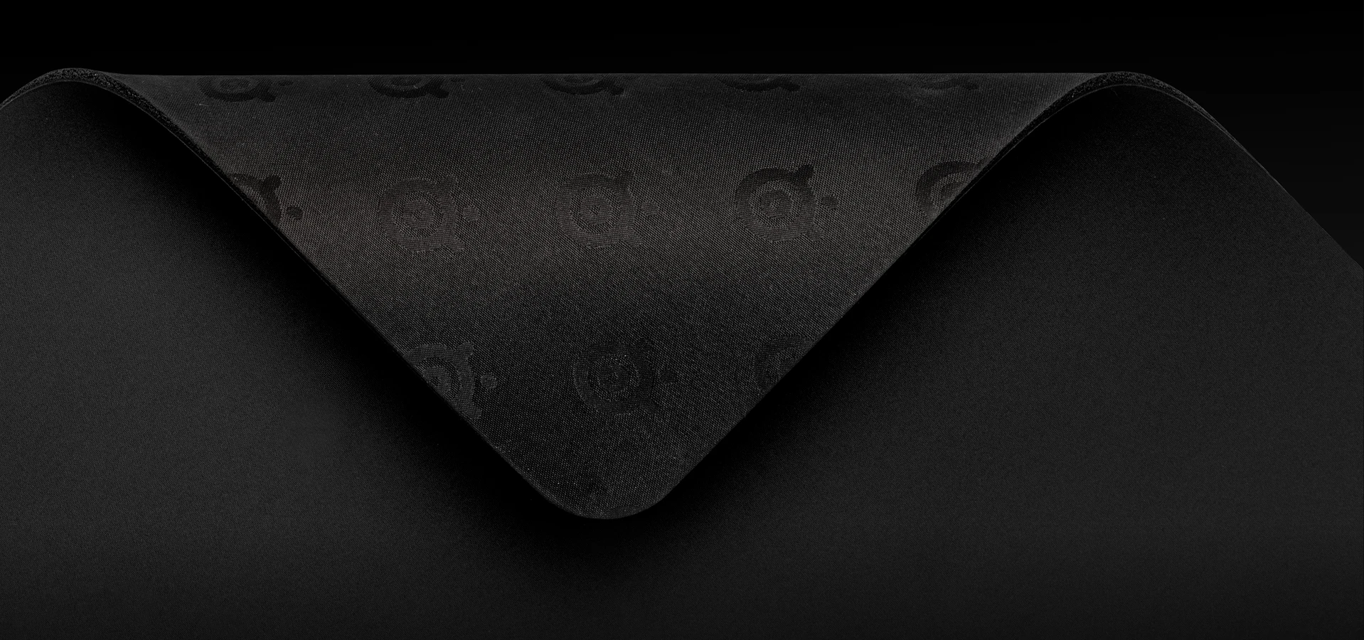Uma foto em close-up do canto de um mousepad preto dobrado para revelar uma base de borracha antiderrapante com o logotipo da SteelSeries em relevo.