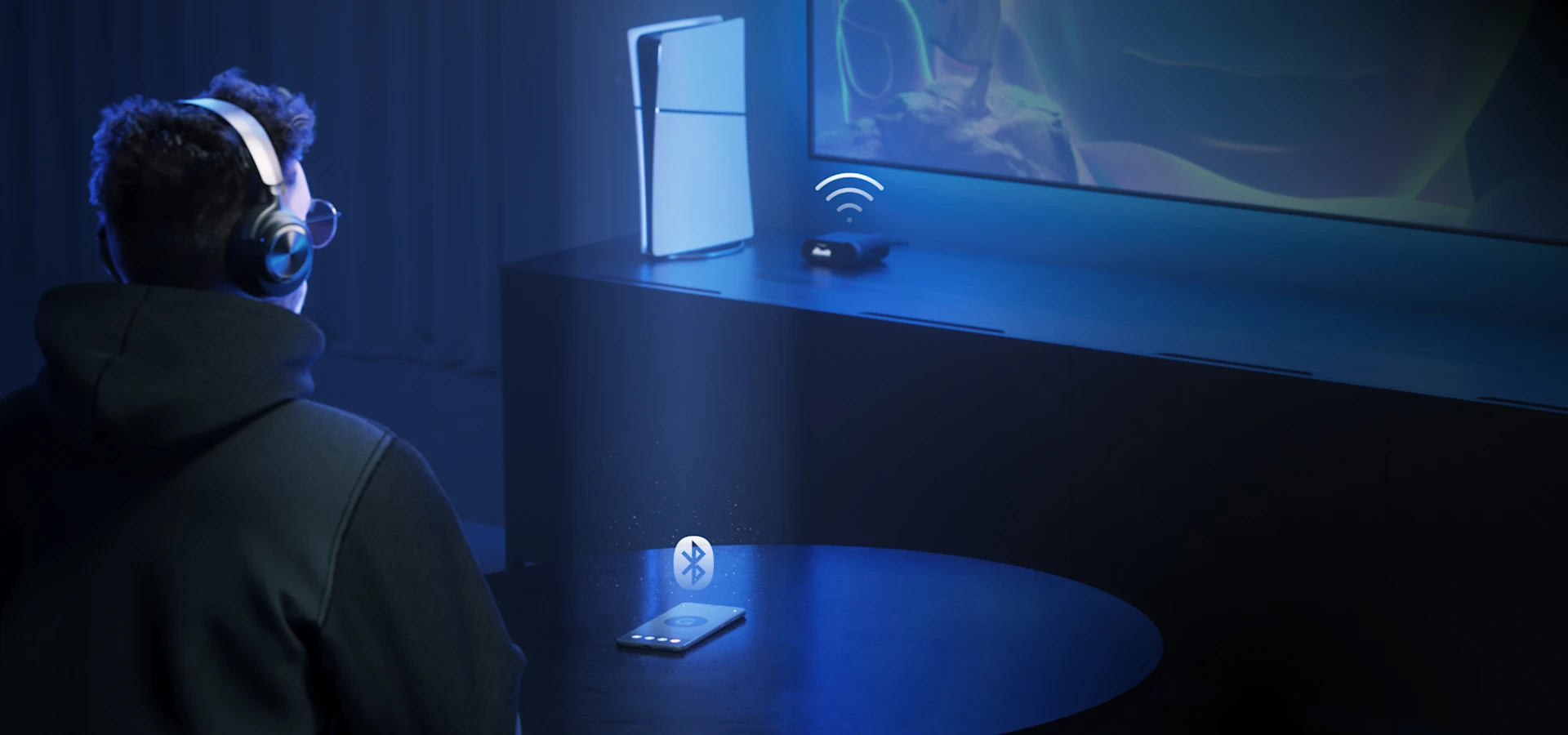 Ein Mann sitzt vor einem großen Fernseher und trägt einen Arctis Nova Pro Wireless-Kopfhörer. Vor ihm auf dem Tisch liegt ein Handy, und auf dem Beistelltisch neben dem Fernseher stehen eine Konsole und eine Kopfhörerstation.