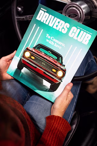 Person holding a “Drivers Club” magazine featuring a red Camaro SS on the cover.