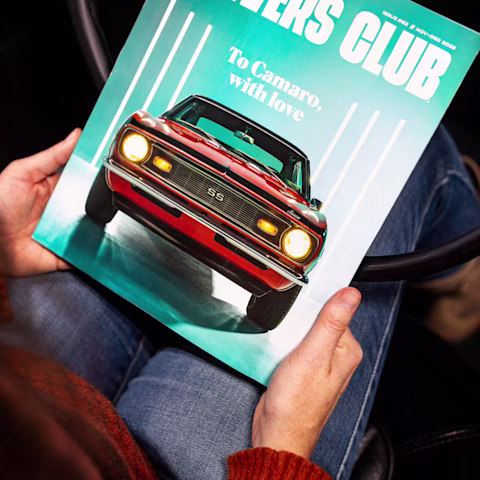 Person holding a “Drivers Club” magazine featuring a red Camaro SS on the cover.